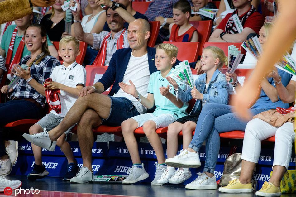 罗本与爱子并肩坐在拜仁篮球馆看台，父子俩神情专注，罗本嘴角挂着轻松的笑意，仿佛正给儿子讲解球场上的战术配合。