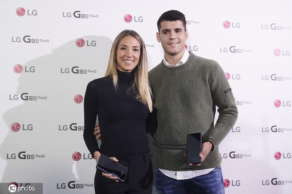 在品牌logo前，莫拉塔轻轻揽住坎佩洛的腰，两人面对镜头露出标准而幸福的微笑，这一刻他们不仅是球星与名模，更是彼此眼中最好的伴侣。