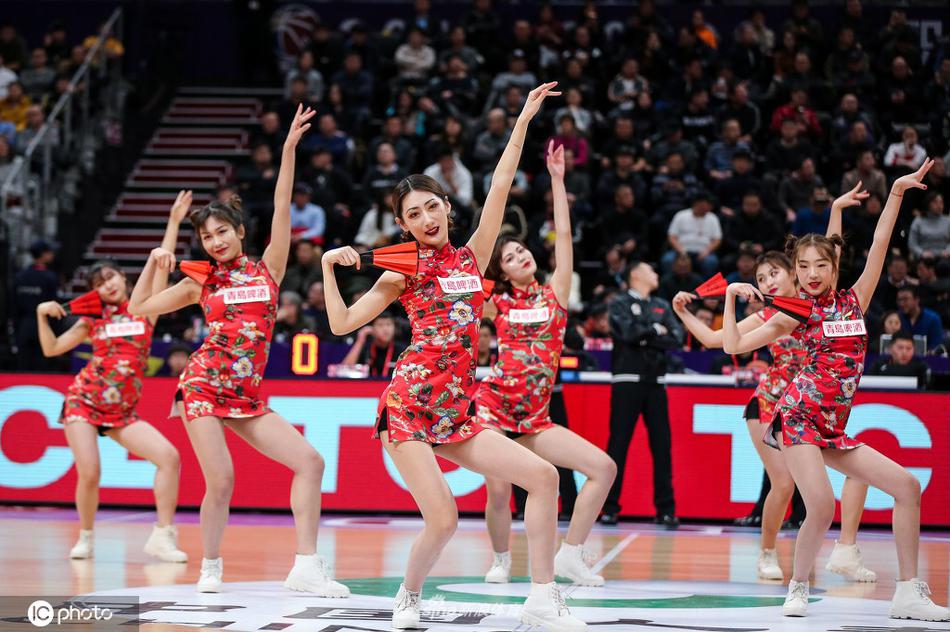 在球场灯光下，一名啦啦队员对着镜头露出灿烂自信的微笑，身后的观众席虚化成斑斓的光点，氛围感十足