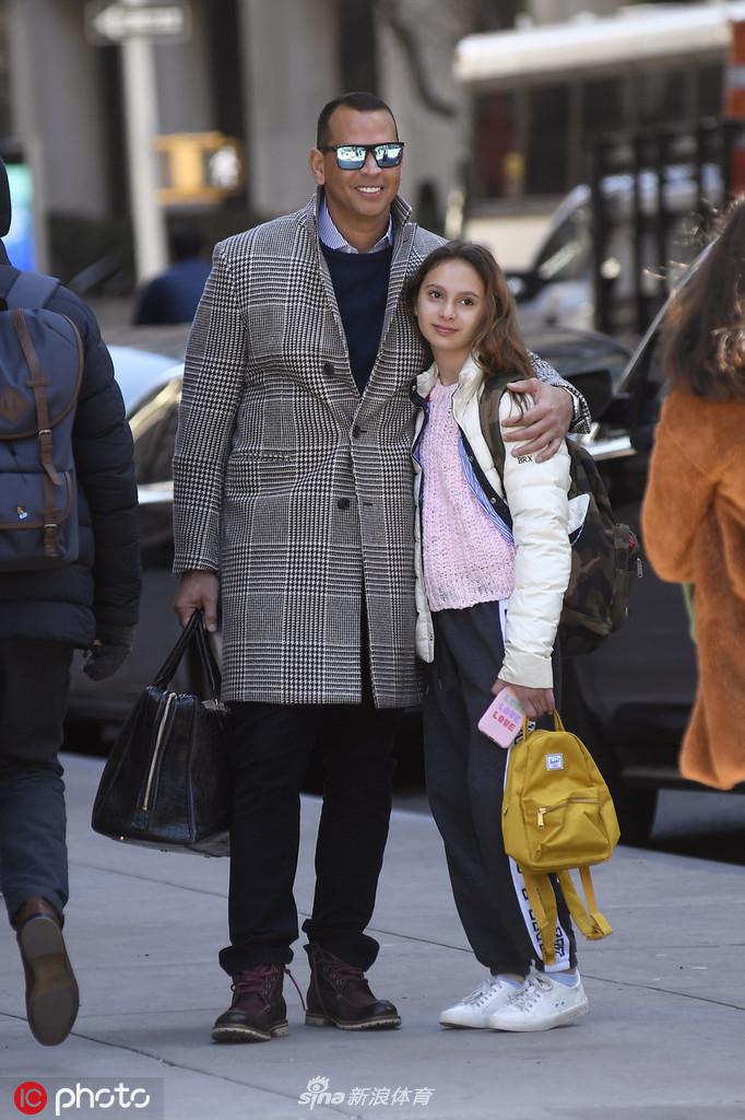 罗德里格斯一手拿着手机，一手指着街边有趣的事物给女儿看，女儿顺着父亲手指的方向好奇张望，父女俩的背影融入纽约的街景之中，构成一幅关于陪伴与探索的温暖画面。