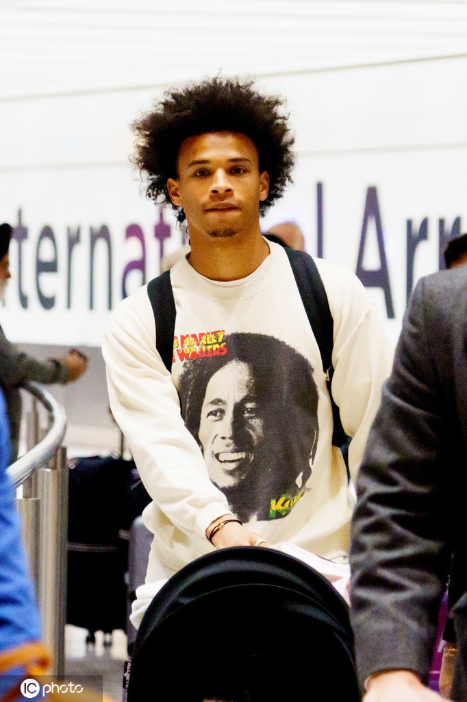 萨内微微弯腰，全神贯注地盯着手机屏幕，身旁是守护着推车的妻子坎迪斯。这短暂的驻足瞬间被镜头捕捉，背景是洛杉矶明亮的日光，一家人的安静等待，仿佛是在积蓄力量，准备告别这段在加州的康复时光，飞越大洋去迎接英超赛场那熟悉的喧嚣与挑战。