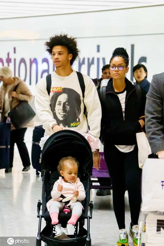 萨内身穿一袭黑衣，用肌肉紧绷的手臂稳稳地将宝贝儿子抱在胸前，父爱如山的沉稳与球场上的灵动形成动人反差，他的眼神温柔地望向怀中的小生命，一旁的妻子坎迪斯则显得轻松惬意，一家三口在洛杉矶机场构成了一道温馨的风景线。