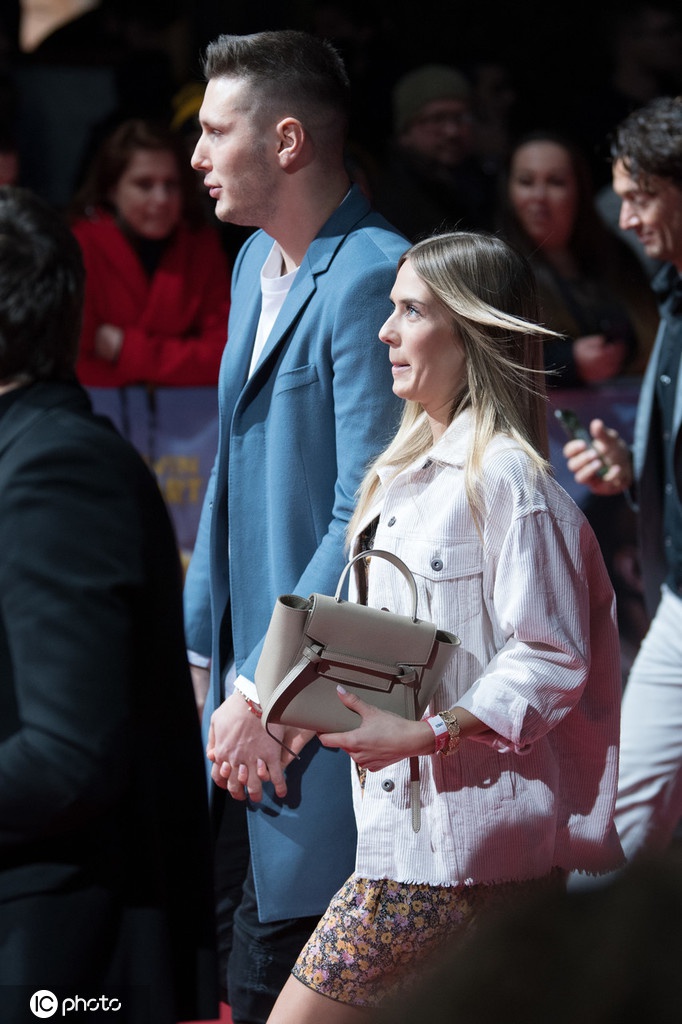 聚勒夫妇在红毯上向周围人群挥手致意，聚勒面带微笑显得轻松自如，女友则挽着他的手臂，显得亲密无间