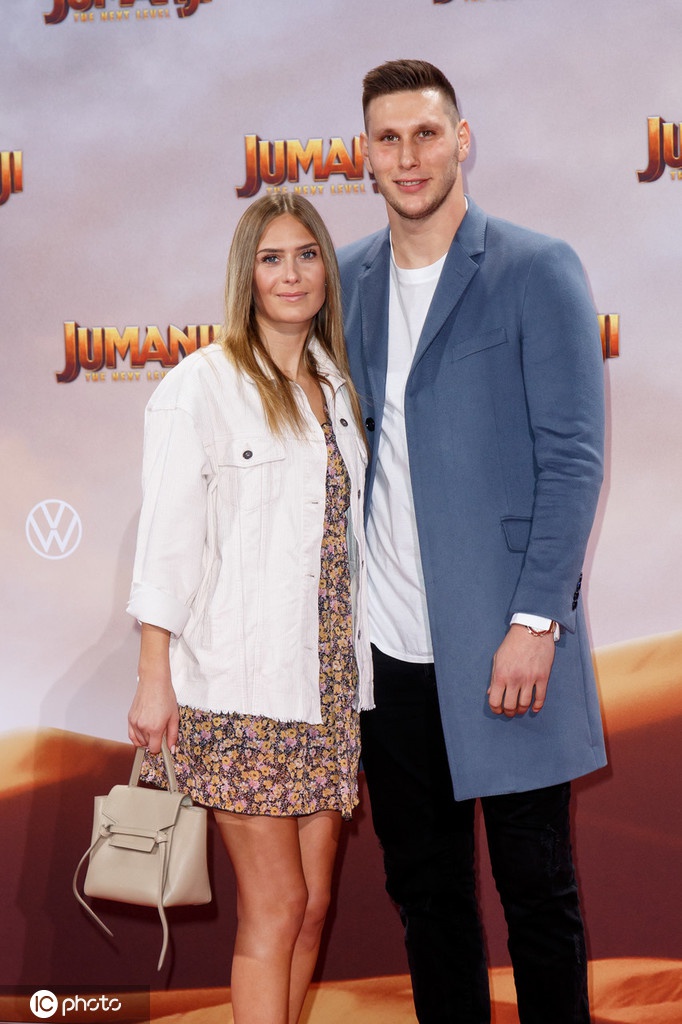 聚勒与女友在电影首映礼背景板前甜蜜合影，他身着深色西装，露出标志性笑容，女友则一袭长裙，两人气质出众