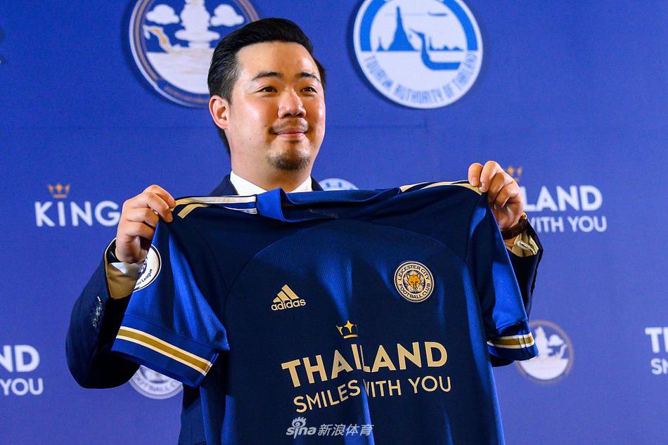 小维猜主席手捧新球衣，脸上洋溢着自豪的笑容，他身后的背景板上，“泰国伴你微笑”的主题与球衣胸前的字样交相辉映，定格下这个充满爱与责任的瞬间。