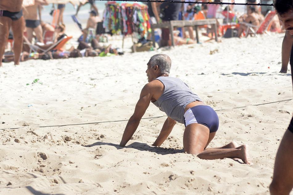 沙滩排球网前，罗马里奥与一位高大的友人展开激烈争夺，他伸展手臂努力拦网，全身肌肉线条分明，力量感十足，仿佛回到昔日与对手后卫争顶头球的时刻。