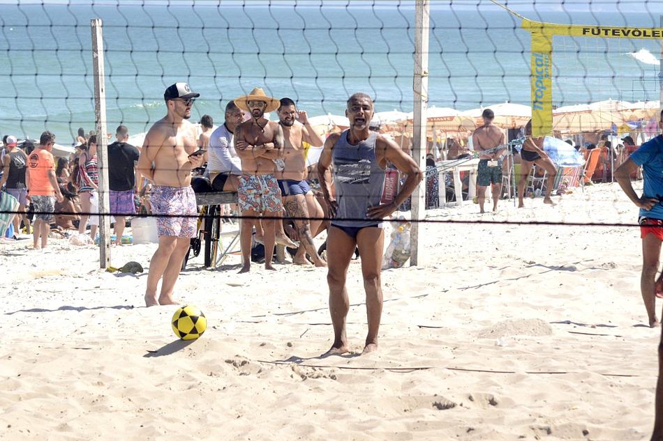 罗马里奥双手垫球后，目送排球飞向队友。他全身肌肉紧绷，姿态稳健，身旁的沙滩上散落着其他休闲的人们，但这片区域仿佛成了他的专属舞台，吸引着周围的目光。