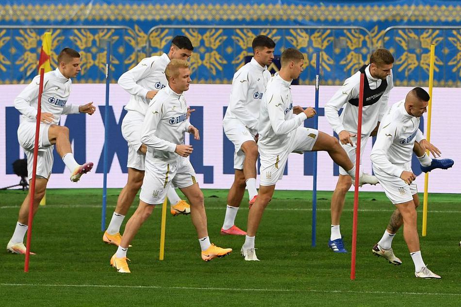 基辅的夕阳洒在训练场上，乌克兰队的球员们正围成一圈，神情专注地聆听着教练组的战术部署，紧绷的肌肉和坚毅的眼神透露出对胜利的极度渴望。