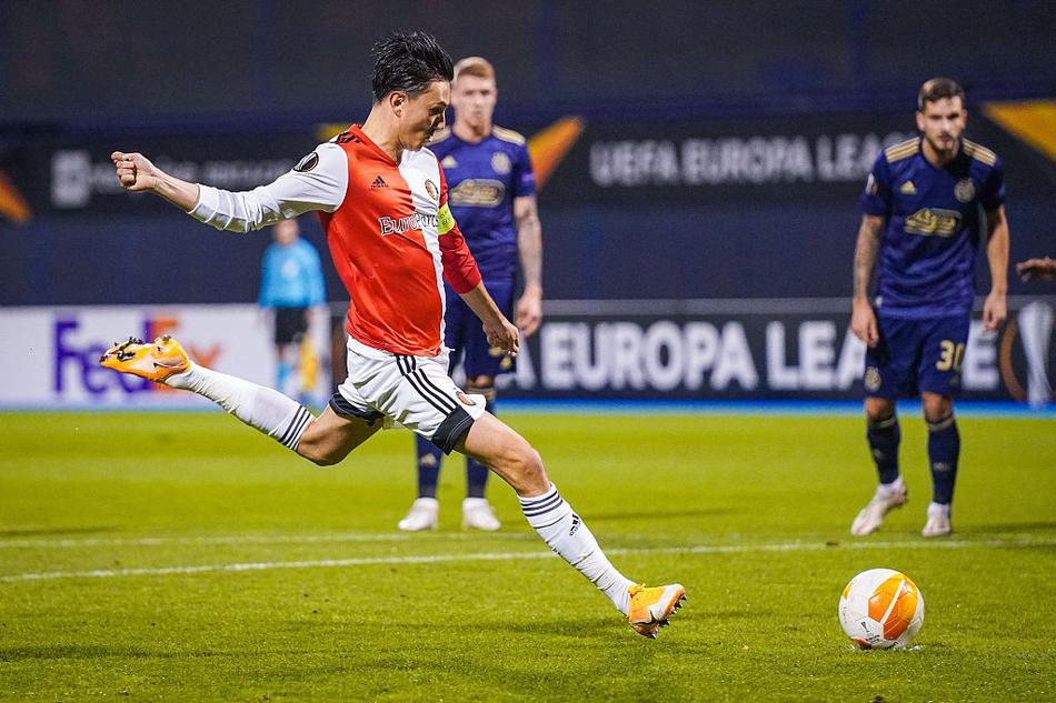 费耶诺德球员在湿滑的草皮上奋力争顶，他身边是贴身紧逼的萨格勒布迪纳摩后卫。两人目光紧锁空中飞行的皮球，手臂张开保持平衡，展现了禁区内令人窒息的防守压力。