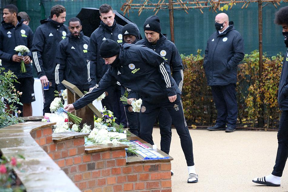 莱斯特城一线队的其他球员们身着便装，排成一行，逐一在维猜的纪念牌前献上黄色与白色的菊花。花瓣上的雨滴晶莹剔透，映衬着球员们脸上的哀伤与坚定。