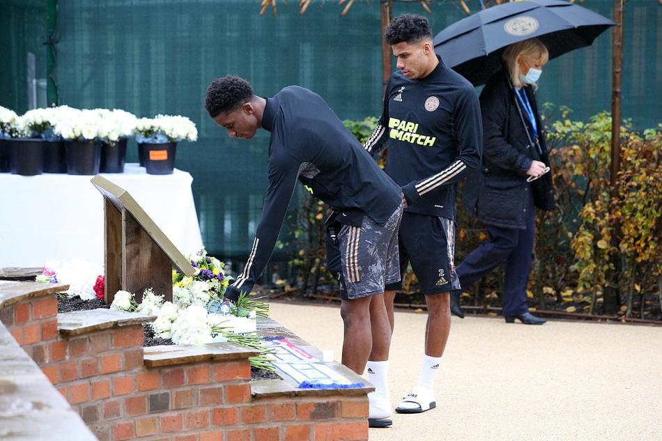 莱斯特城俱乐部首席执行官苏珊·惠兰与主教练布伦丹·罗杰斯并肩而立，手持洁白的鲜花，低头默哀。他们的身后是修剪整齐的灌木，代表着俱乐部管理层对前任主席的承诺与继承。