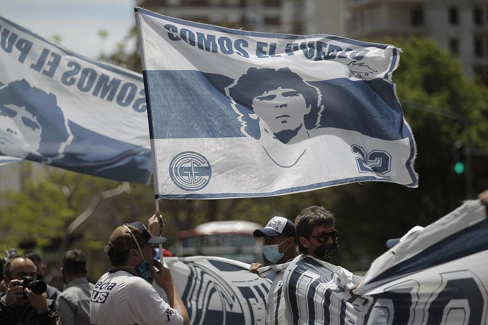 神情坚毅的马拉多纳在保镖守护下，身披深色外套缓缓步入医院，面对镜头挥手致意，仿佛在告诉全世界不必为他担心