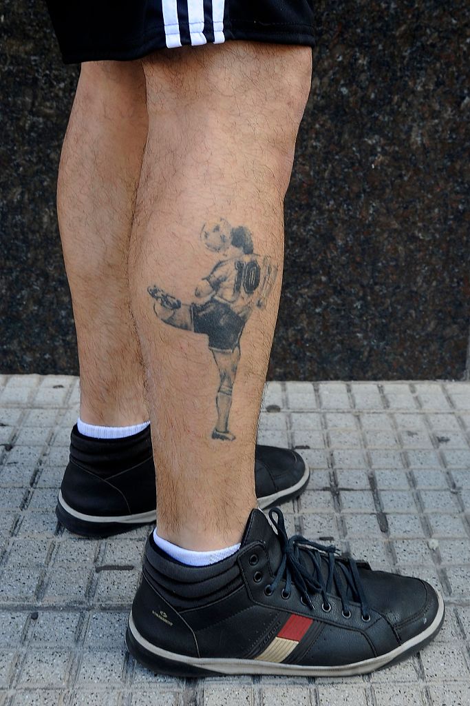 一位戴着口罩的老年女球迷难掩内心的激动，她双手紧紧合十放在胸前，双眼微闭，虔诚地为手术室中的马拉多纳向上天祈祷