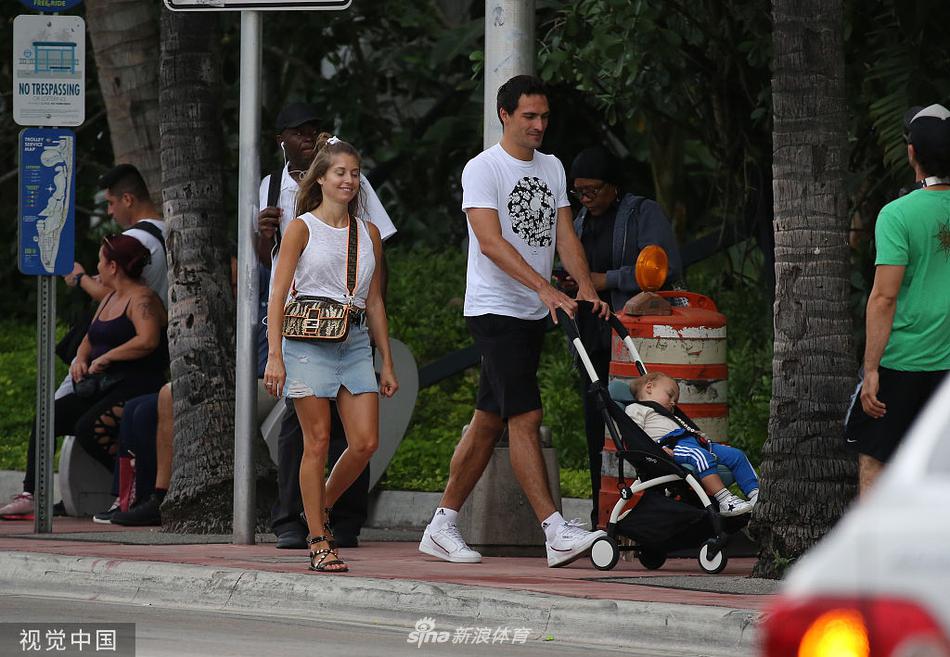 正午的树荫下，胡梅尔斯一家坐在野餐垫上，凯茜正低头为儿子整理小帽子，胡梅尔斯则侧身看着他们，目光柔和，画面静谧得能听见海风穿过树叶的沙沙声。