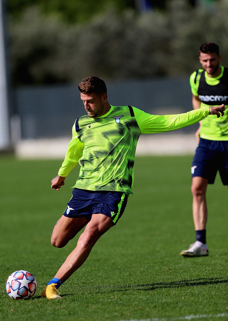 一名拉齐奥球员正在进行高空球停球练习，他舒展身体，用胸部优雅地将球卸下。背景是训练场的围栏和稀疏的树木，整个画面如同一幅静态的油画，定格了大战前夕的宁静与专注。