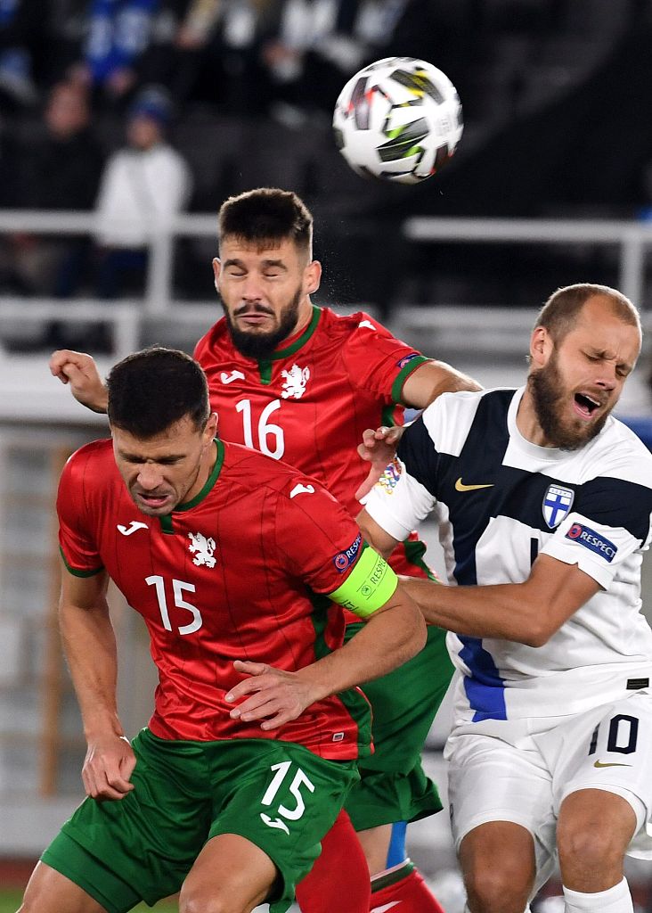 芬兰前锋在对方禁区腹地，于两名保加利亚防守球员的夹击之下，高高跃起争顶头球，他舒展的身姿与紧绷的肌肉线条，充分展现了力与美的结合，预示着球场上每一次进攻机会都弥足珍贵。