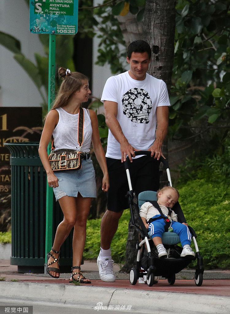 小家伙光着脚丫，专心致志地堆砌着他的沙堡王国，胡梅尔斯则单膝跪地，用一根手指轻轻指点，仿佛在为儿子规划最稳固的防线，父子俩的脑袋几乎要碰到一起。