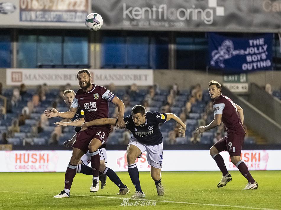 米尔沃尔年轻前锋特洛伊·帕罗特半场被换下后坐在替补席，神情落寞，他的英联杯首秀以遗憾告终，身后是喧嚣的球迷看台。