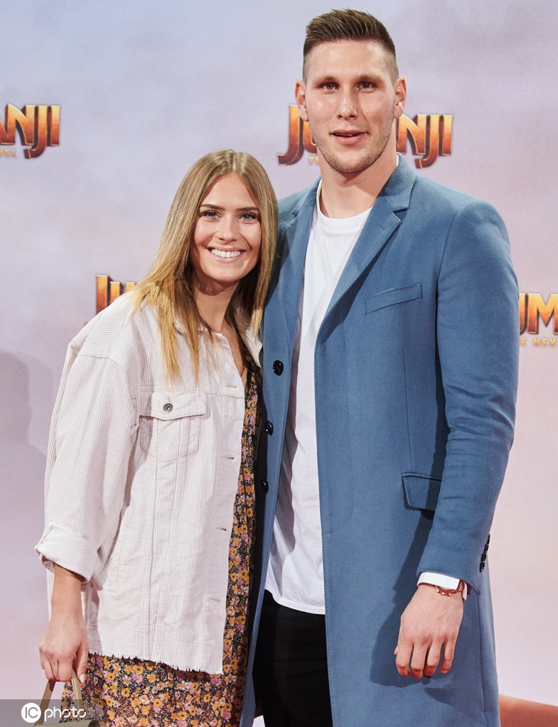 聚勒的女友单独在电影背景板前留影，她身穿设计感十足的礼服，面对镜头露出迷人的微笑，气质优雅