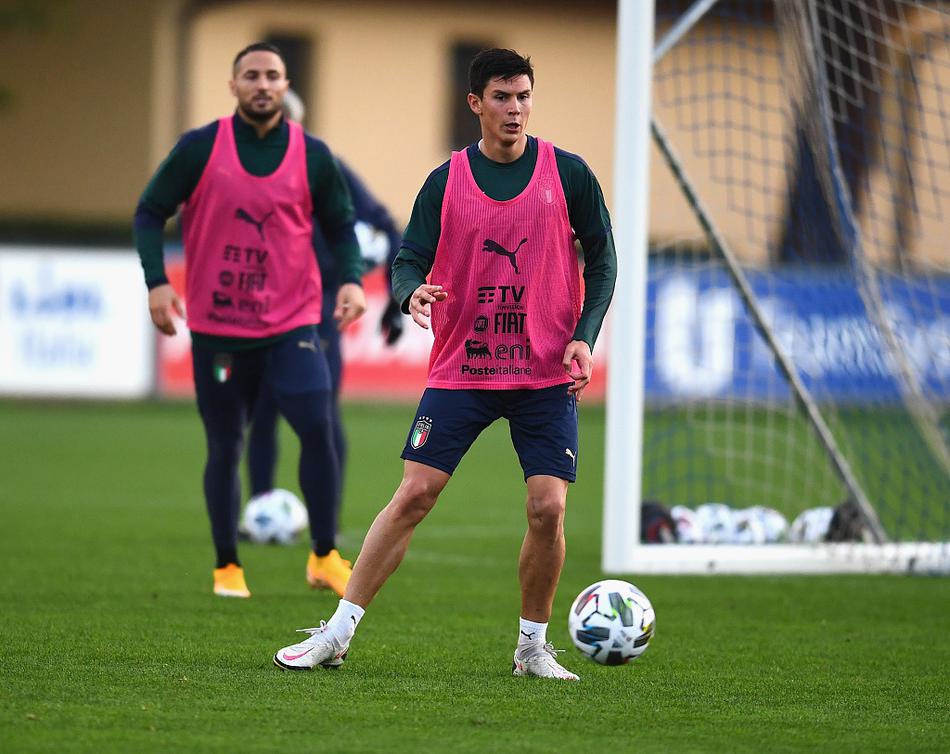 战术板前，意大利的教练团队正通过手势和模型向球员们布置针对性战术，背景中隐约可见的队友身影，预示着新老交替的传承。