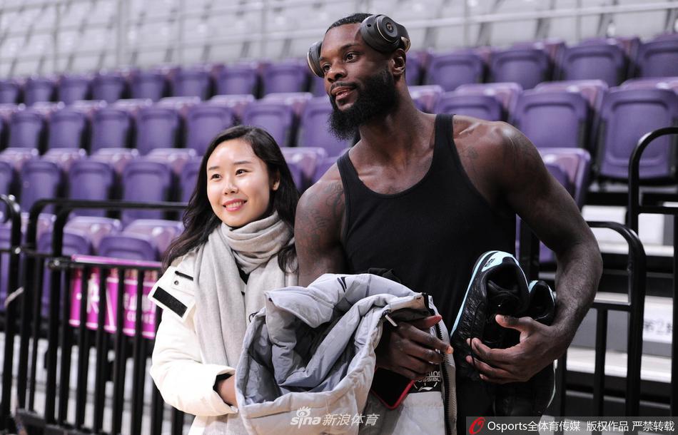 辽宁队外援巴斯面带标志性的憨厚笑容，双手捧着一件球迷递来的球衣，眼神专注地为面前的小朋友签名，周围的相机闪光灯记录下了这温馨的一刻。