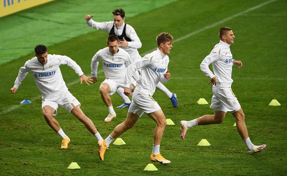 夕阳的余晖洒在训练场上，一名乌克兰球员正在单独练习传中球。他反复调整着步伐，将皮球精准地送入禁区内的指定区域，教练员则在一旁大声提醒着跑位的时机与弧度。