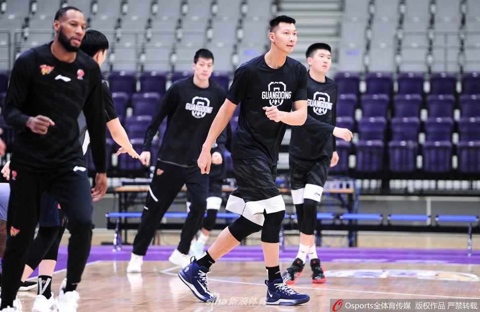 主帅杜锋双手插兜站立，神情严肃地观望场内训练，旁边工作人员正整理训练器材。