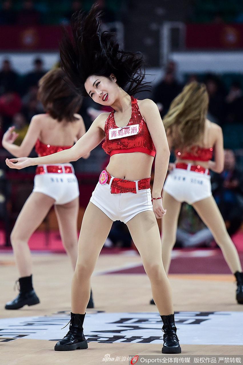 一位篮球宝贝双手紧握红色拳套置于胸前,眼神坚毅地凝视镜头,背后的虚化背景中,是正在热身的山西队球员,她仿佛化身为了守护主场的“美女拳王”。