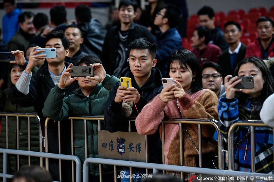 在球员通道旁，一位戴着眼镜、气质清新的女球迷被镜头聚焦，她面带微笑注视着前方，背景是模糊的赛场灯光，仿佛一位忠实的见证者，用安静的目光陪伴着球队走过每一场战斗。