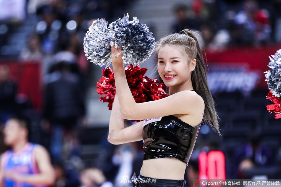 镜头拉近，这位啦啦队宝贝的笑容格外甜美，她眼神专注而明亮，手中的花球仿佛也被她的热情感染，在聚光灯下划出一道道金色的光弧。