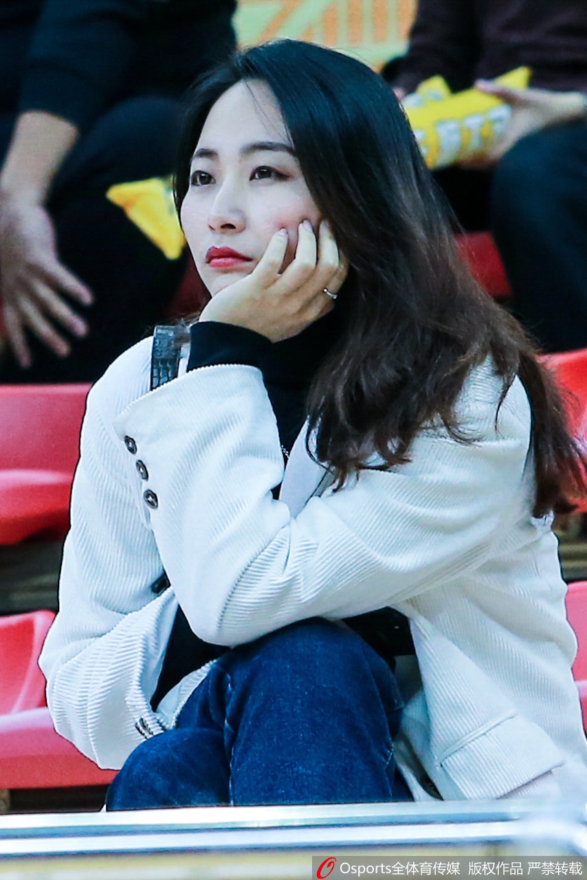 看台之上，一位面容清秀的美女球迷轻抿嘴唇，双手轻放在栏杆上，眼神中流露出一丝紧张与期待，她仿佛与场上激烈的拼抢同呼吸，完全沉浸在这属于篮球的夜晚之中。