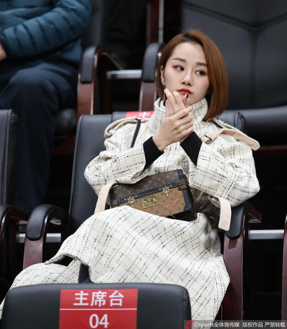 一位妆容精致的女球迷坐在看台上，她身披辽宁队外套，目光专注地追随着场上的球员，在喧闹的场馆中显得格外文静而投入。