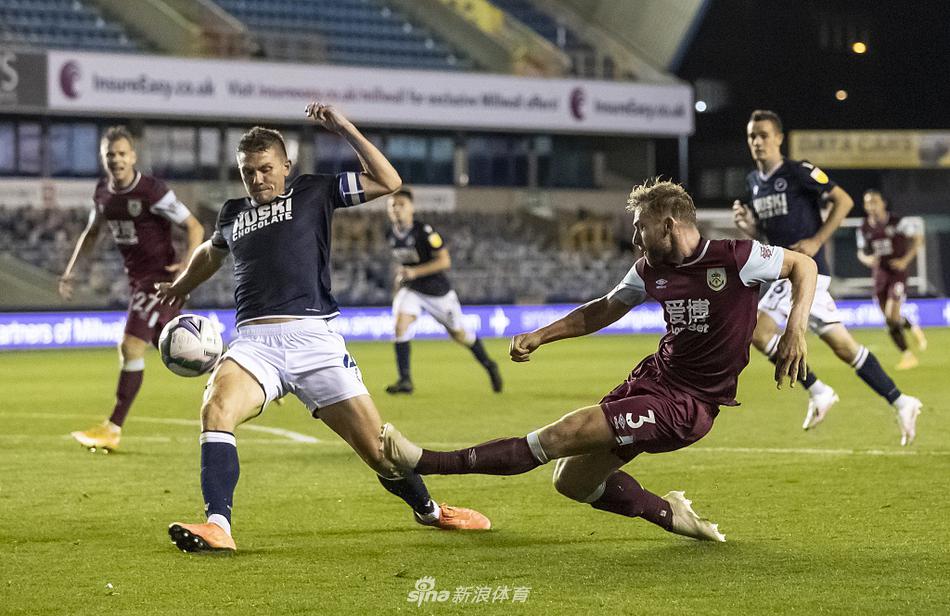 尼尔球场夜幕下的激烈拼抢，米尔沃尔与伯恩利球员在雨中展开英联杯争夺，草皮上水花四溅，氛围紧张。