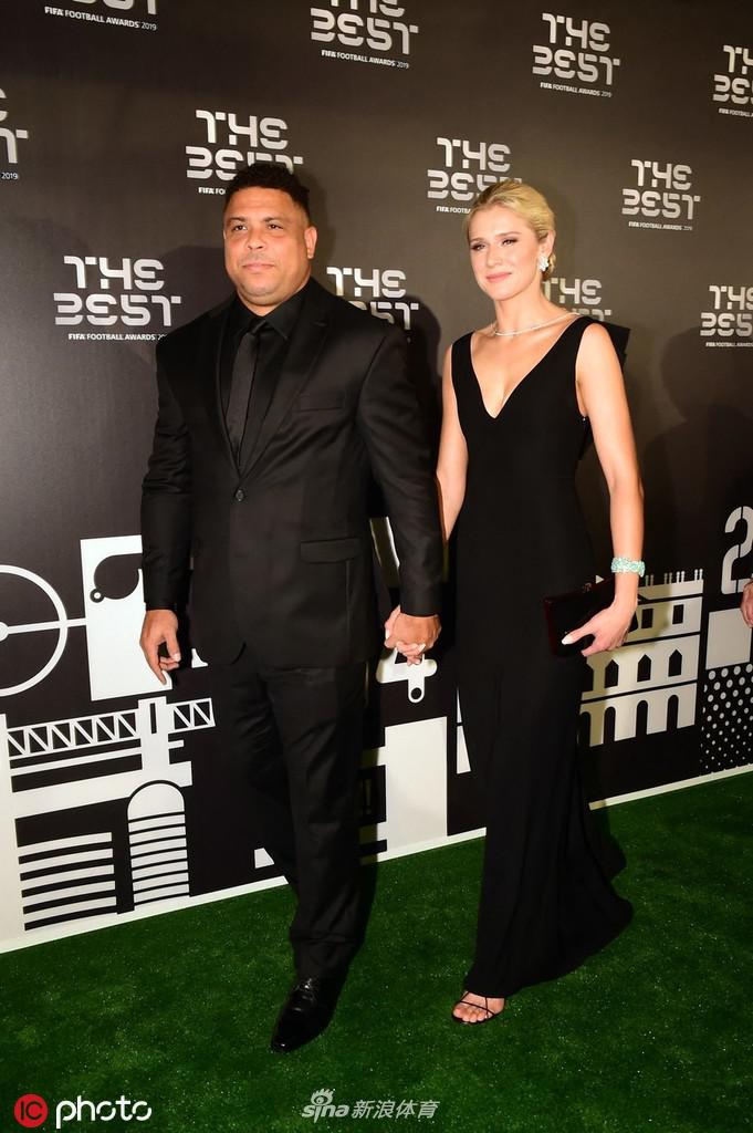 女伴的浅色礼裙在红毯上格外亮眼，她挽着大罗的手臂，两人步伐一致，走向采访区，身后是庄严典雅的米兰建筑背景。