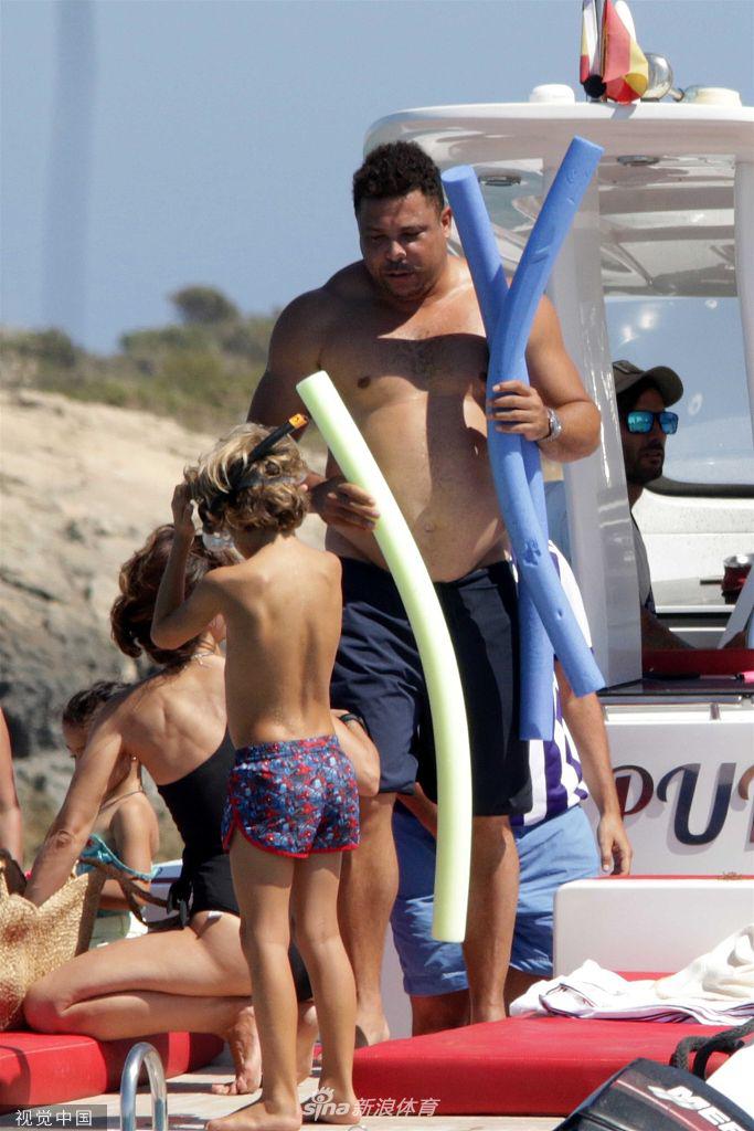 罗纳尔多在游艇上拿着饮料，表情惬意，身上的肉感与手臂的壮实感并存，背景是西班牙蔚蓝的海岸线