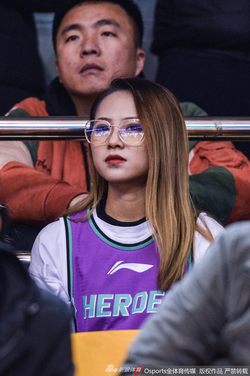 一位气质文静的女球迷侧身面对镜头，她将手中的加油棒轻轻贴在脸颊，眼神穿过人群投向远方，仿佛在默默祈祷，希望心中的英雄能在下一次进攻中创造奇迹。