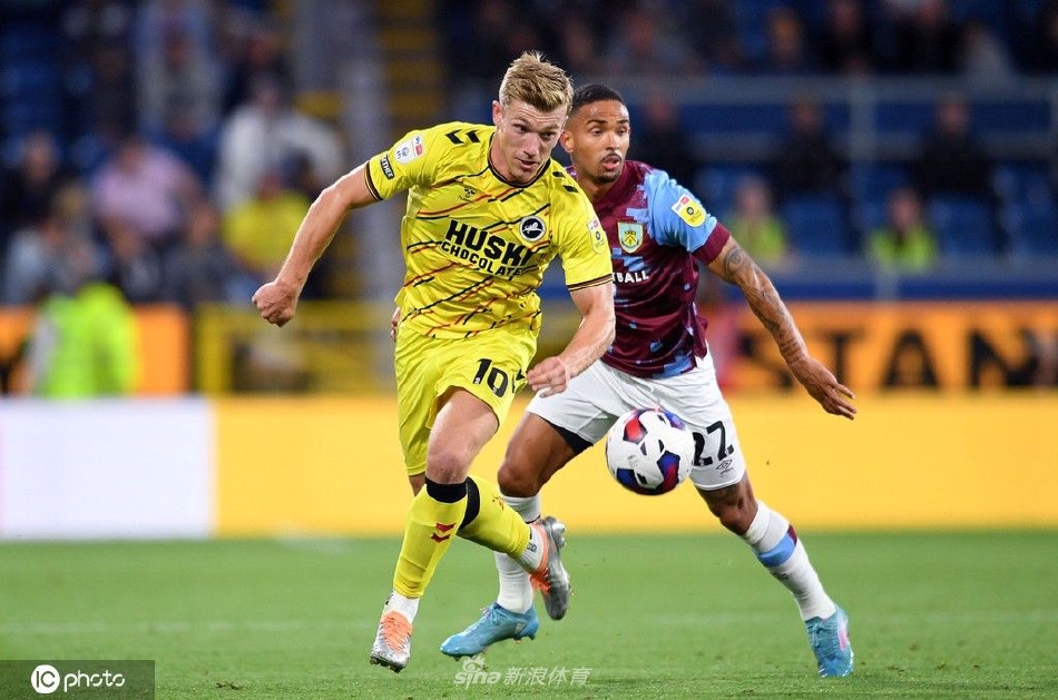 米尔沃尔球员奋力跃起争顶头球，肌肉紧绷充满力量感，背景是焦急注视的伯恩利防守球员