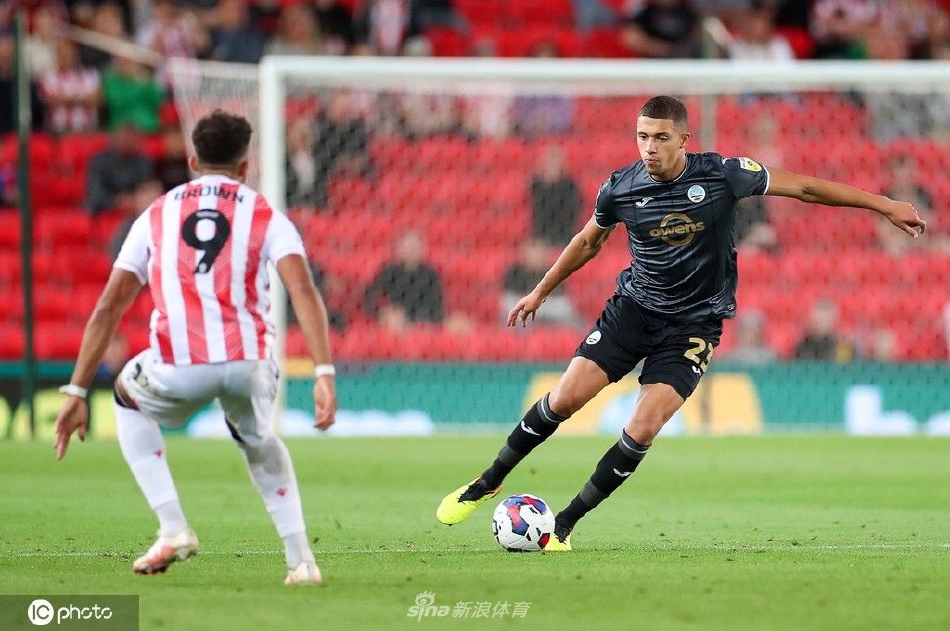 看台上的斯托克城小球迷身穿雨衣，脸上涂着队徽油彩，眼神充满期待与激情，他是俱乐部未来的希望与传承。