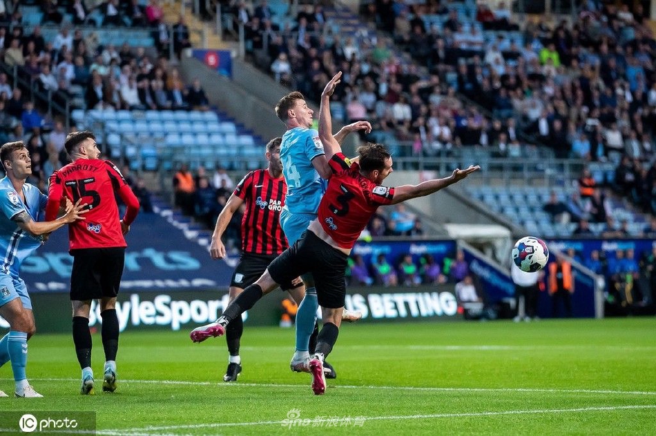 考文垂球员在普雷斯顿禁区内抢点攻门，对方门将弗雷迪·伍德曼飞身扑救，手臂伸展到极限。