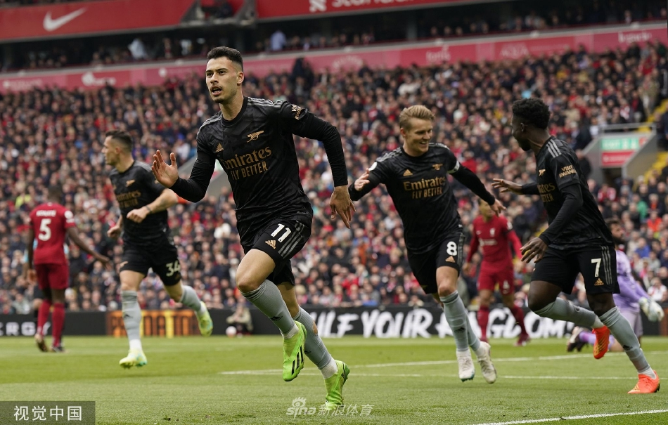 安菲尔德球场全景，看台上红色浪潮翻涌，两队球员在中场激烈拼抢，气氛紧张而热烈。