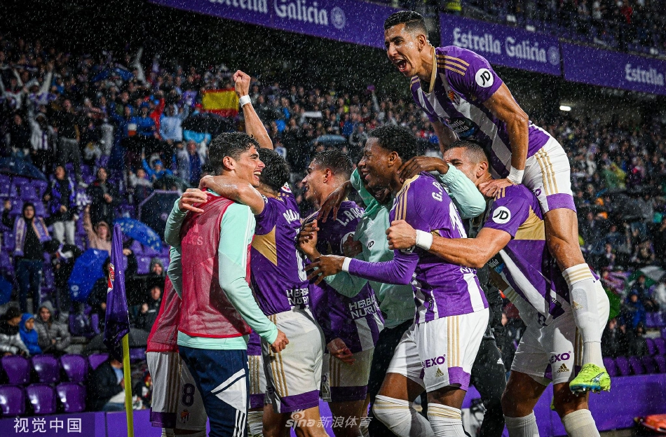 双方球员在中场展开激烈拼抢，球鞋与草皮摩擦扬起碎屑，瞬间的对抗充满了力量与竞技的张力。