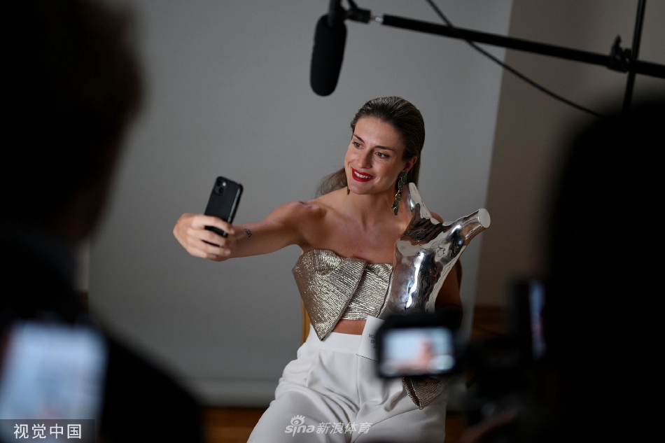 普特拉斯身着优雅礼服侧身站立，奖杯的光芒映照在其坚毅而柔和的脸庞上