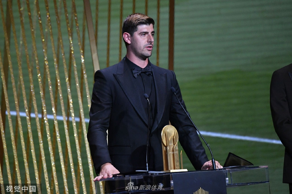 库尔图瓦身着优雅西装，在聚光灯下高举雅辛奖杯，奖杯的光芒与他自信的目光交相辉映。