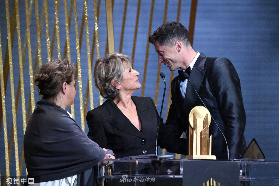 莱万与身穿蓝色西装的加维在典礼现场互动，莱万眼神慈祥如前辈，轻拍加维手臂，而年轻的加维则报以尊敬的笑容，画面温馨，寓意着巴萨队内的传承与团结。