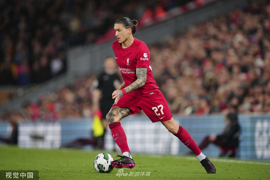 利物浦主帅克洛普在场边神情专注，双臂交叉于胸前，他注视着场上局势，身后的替补席和观众席构成了一片红色的背景。