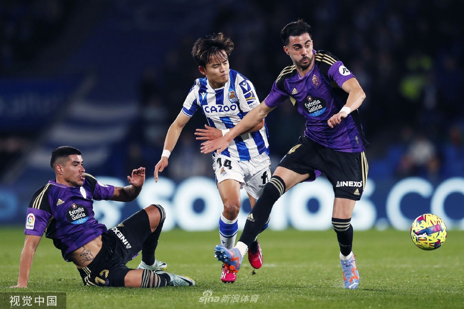 皇家社会球员久保建英带球突破，身旁两名巴拉多利德防守球员紧追不舍，形成激烈的身体对抗。