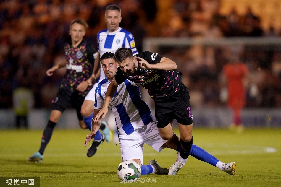 布伦特福德球员进球后张开双臂，面向随队远征的客队看台激情庆祝，与身后略显失落的科切斯特联后卫形成鲜明对比。