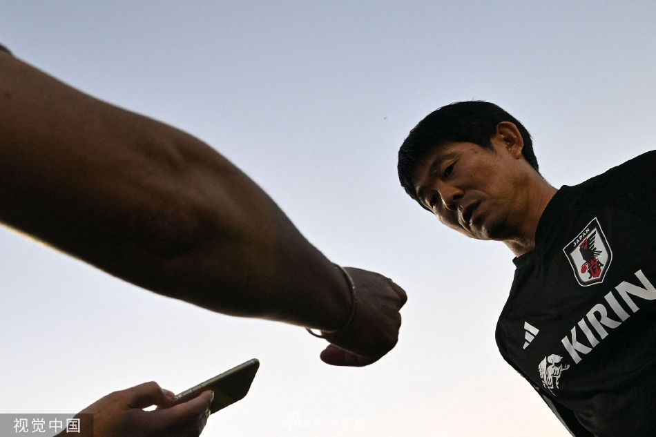 主教练森保一神情专注，手持战术板，在训练场边向核心队员低声布置关键战术，夕阳将他们的影子拉长。