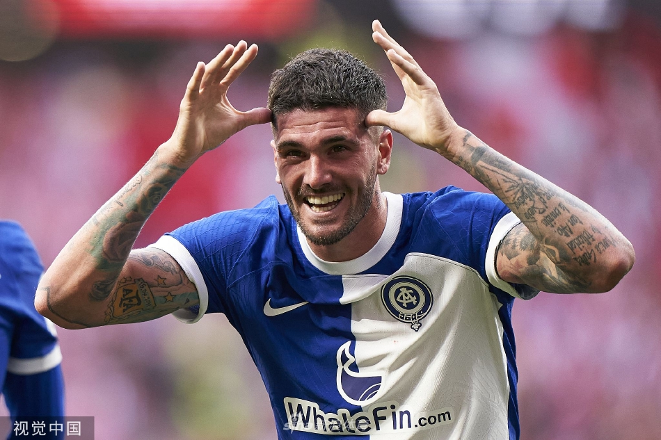 马竞球员激情庆祝进球，众人相拥，红色战袍在绿色草甸上宛如胜利的火焰。