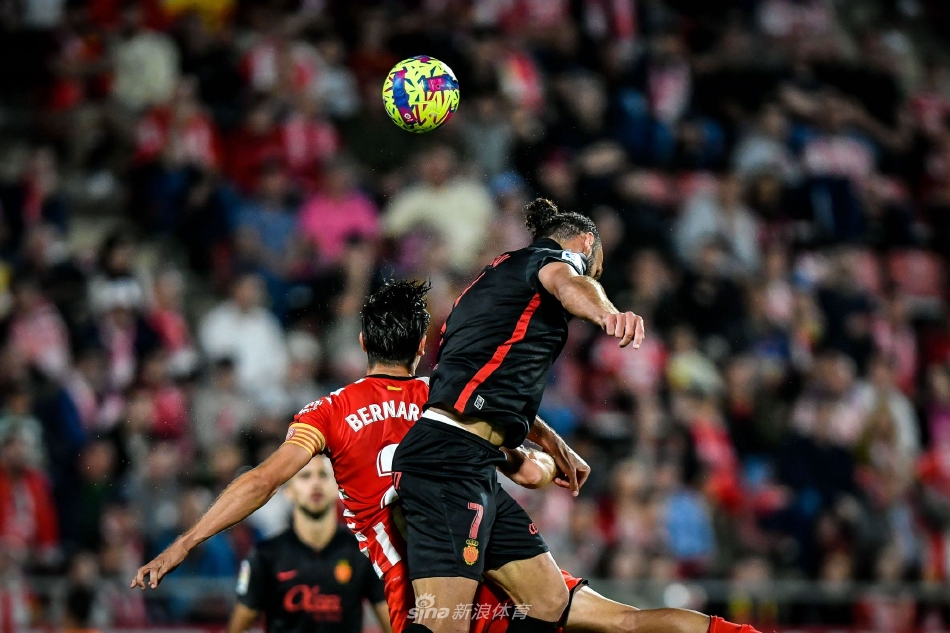 赫罗纳球员庆祝进球瞬间，进球者张开双臂奔向角旗区，身后队友飞扑而来准备拥抱，看台上球迷挥舞围巾形成红色海洋